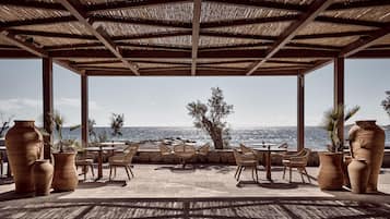 An outdoor seating area with tables and chairs, overlooking a body of water.
