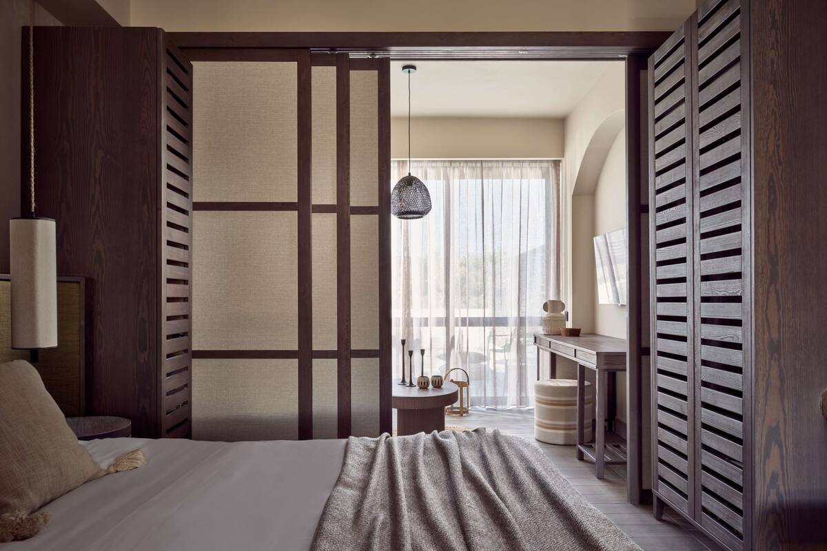 A hotel room with a bed, a desk, a chair, and a view of the outdoors.