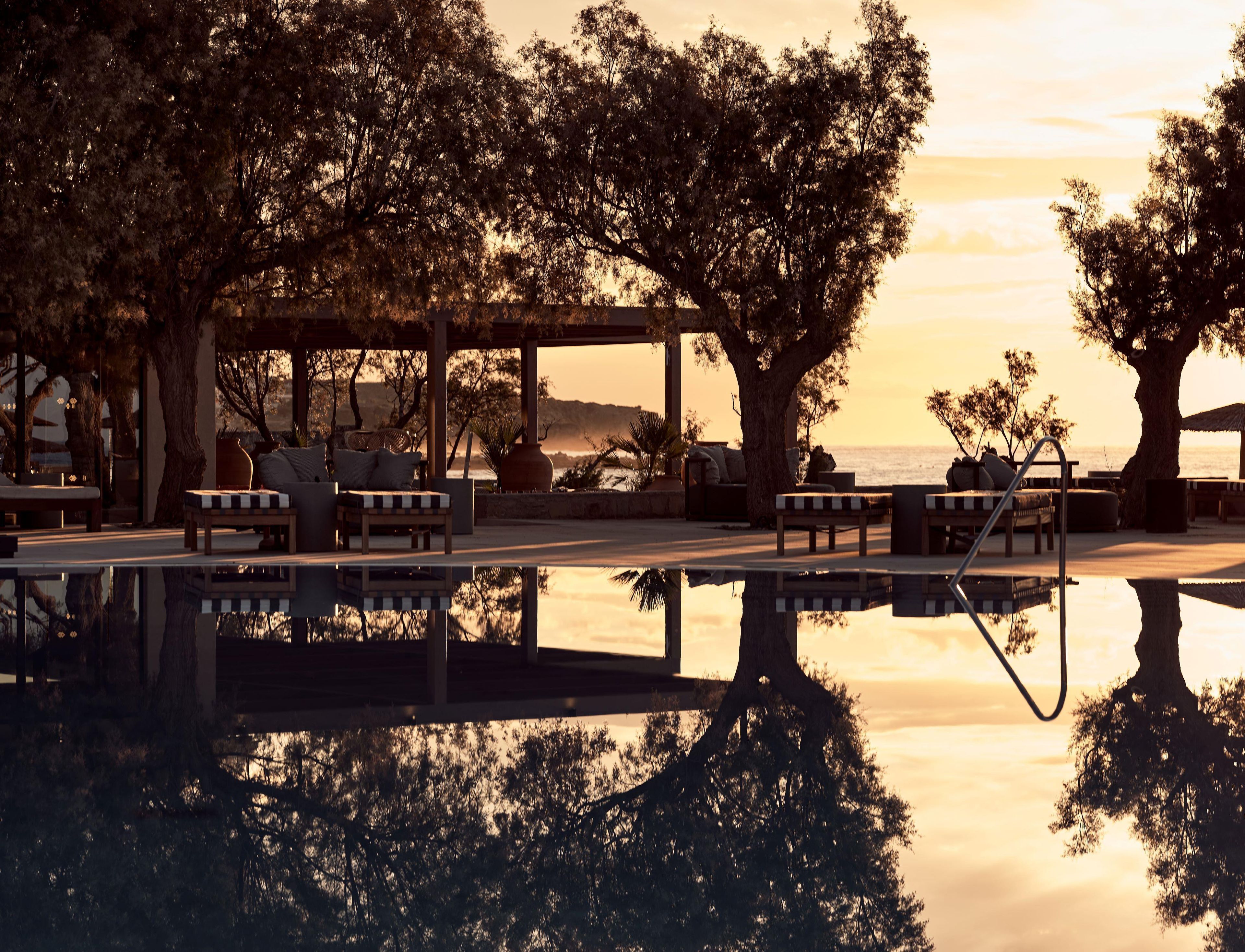A serene outdoor seating area with a pool reflecting trees and a sunset.