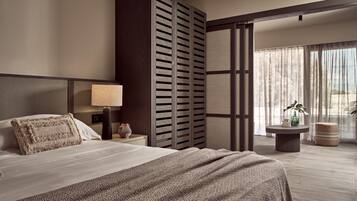 A modern hotel room with a large bed, a bedside table with a lamp, a decorative vase, and a view of the outdoors through sheer curtains.