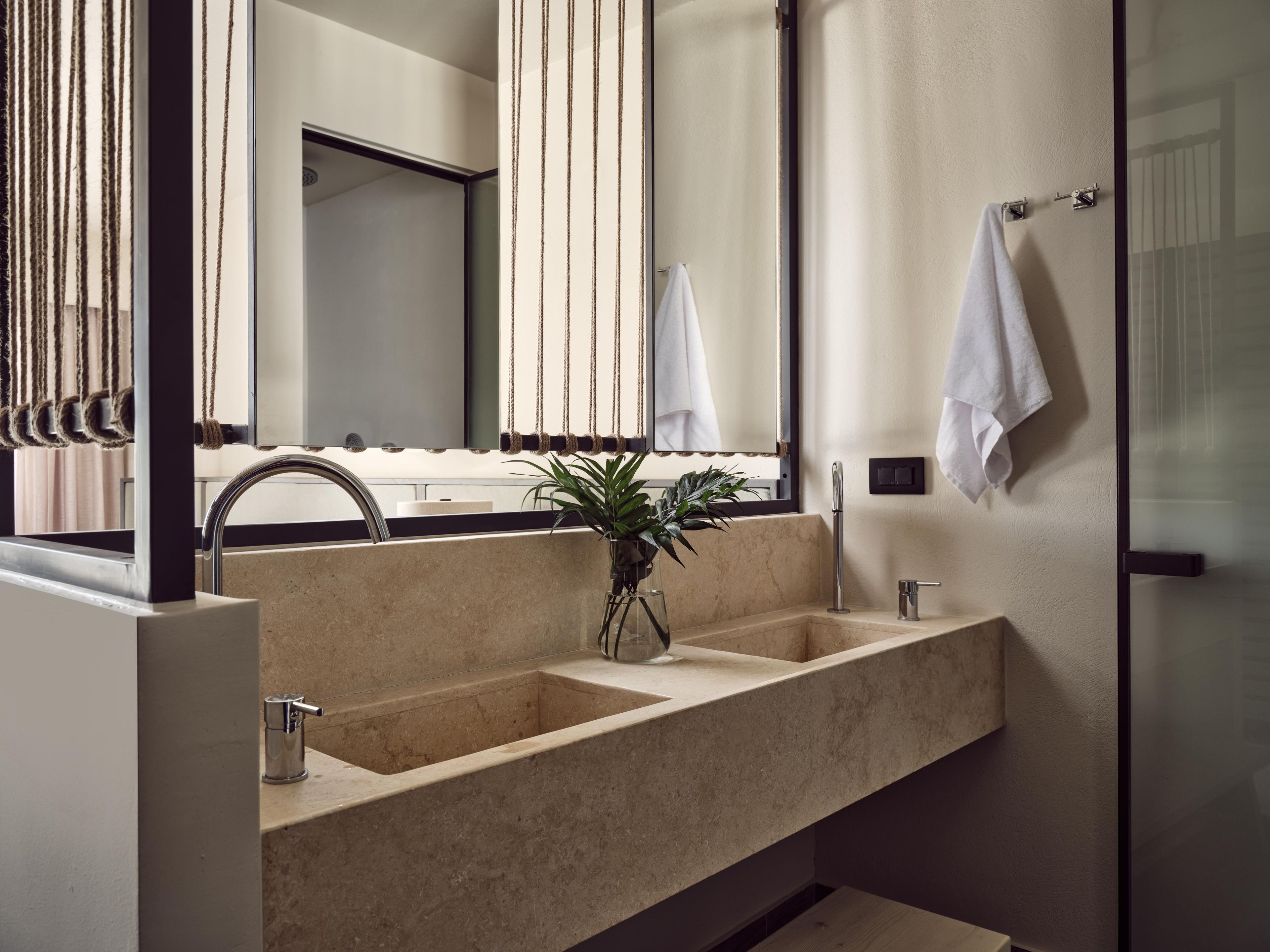 A modern bathroom with a large mirror, two sinks, and a potted plant.