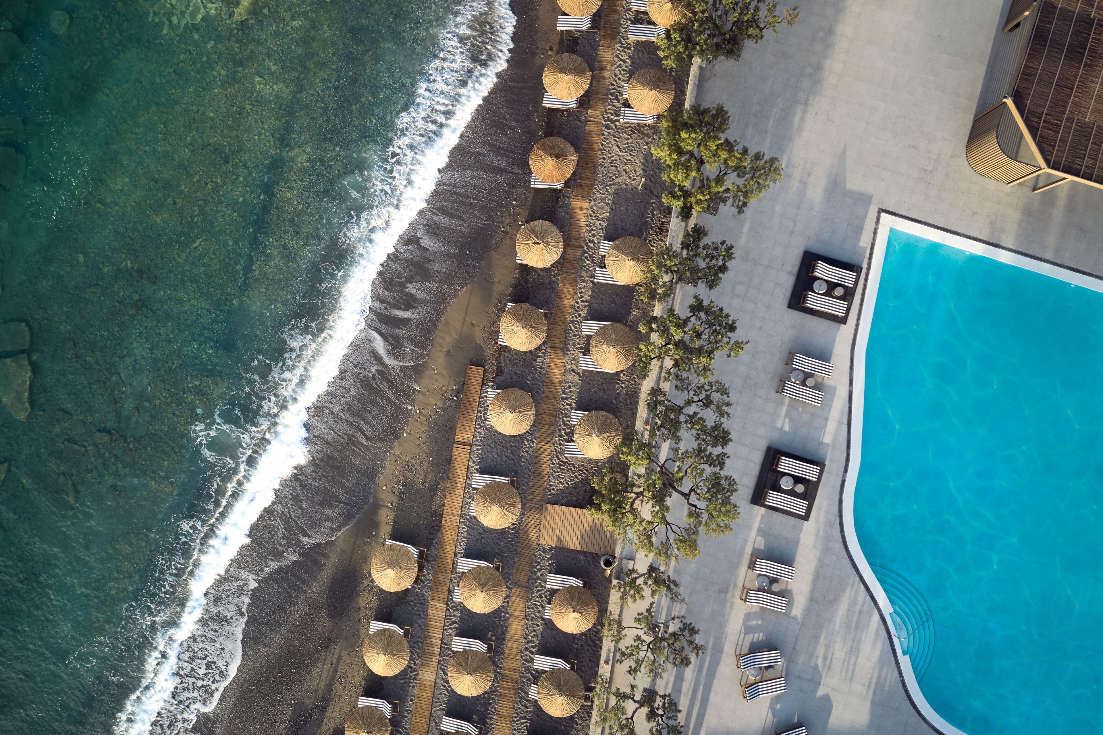 An aerial view of a beachside resort with a swimming pool, sun loungers, and umbrellas.