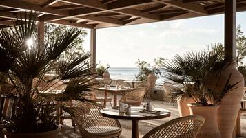 An outdoor seating area with wicker chairs and tables, overlooking a body of water.