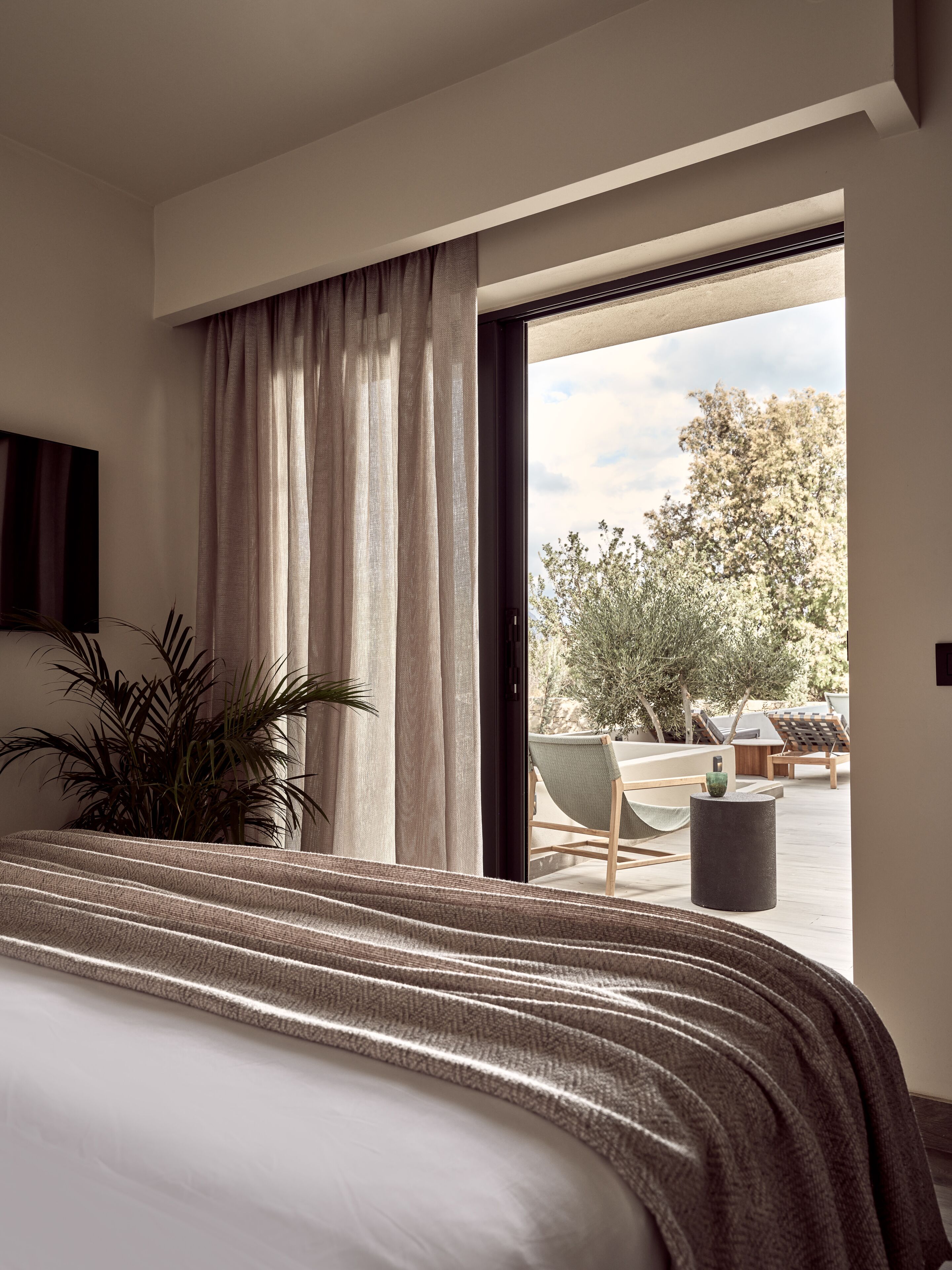 Ein Schlafzimmer mit einem großen Bett, einem Blumentopf und Blick auf einen Außenbereich mit Stühlen und einem Tisch.
