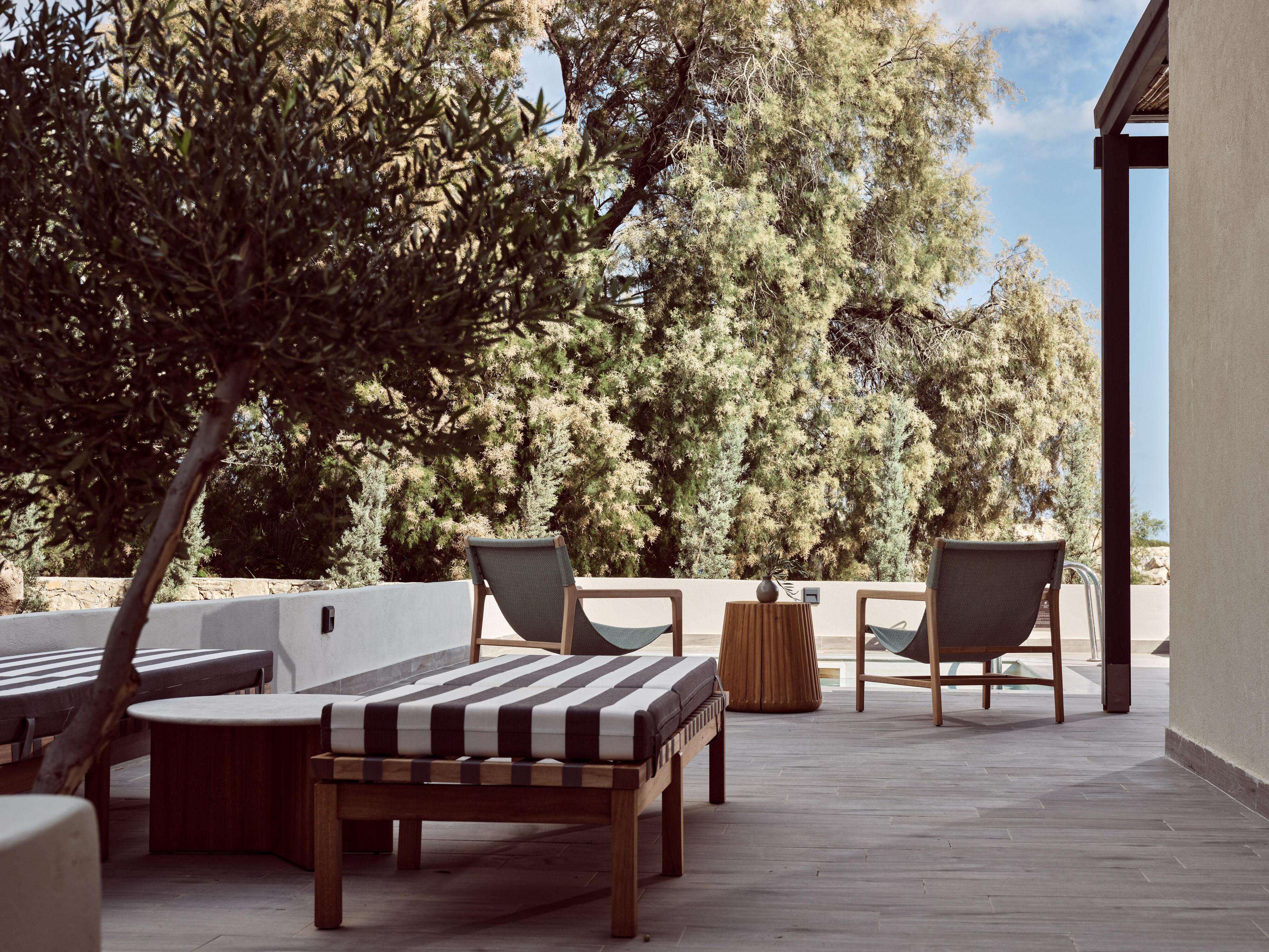 Een terras met een houten bank, twee stoelen en een kleine ronde tafel.