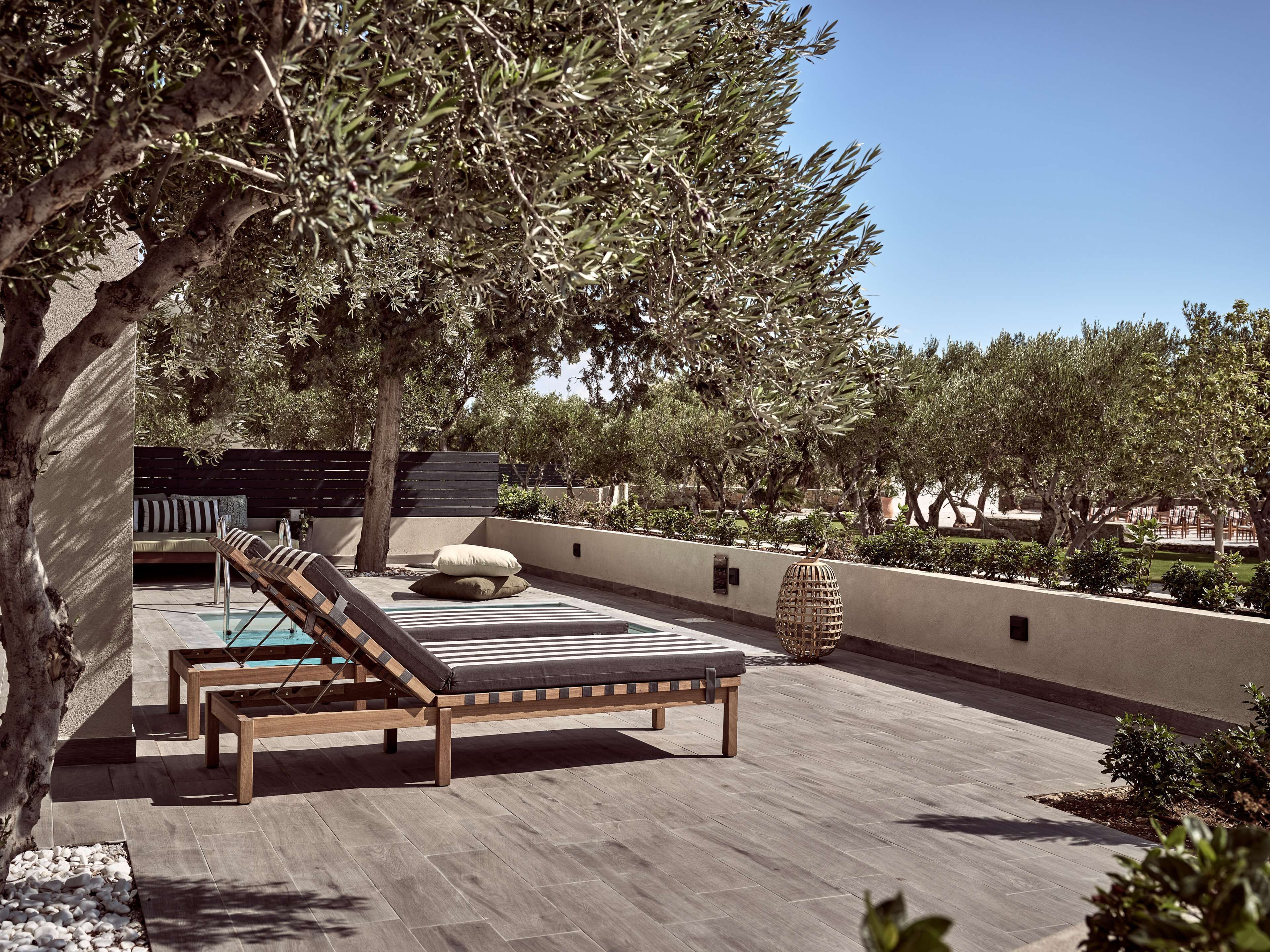 A rooftop terrace with a wooden lounge chair, a small table, and a pool.