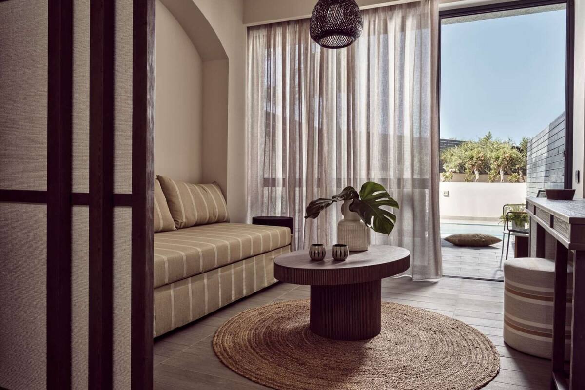 A modern living room with a sofa, a round coffee table, and a view of a pool and greenery outside.