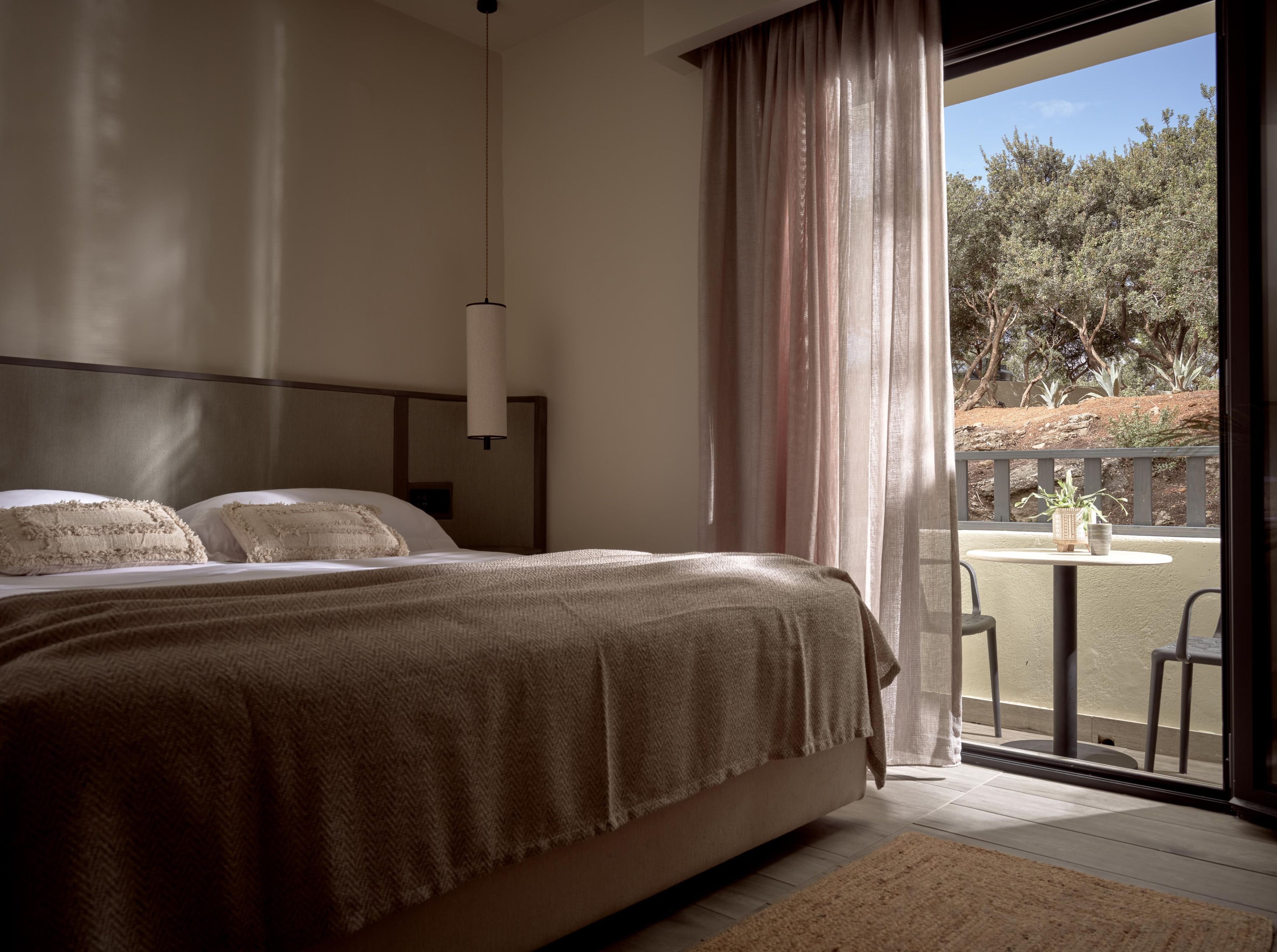 Une chambre avec un grand lit, une table de chevet et une vue sur un patio aménagé avec une table et des chaises.