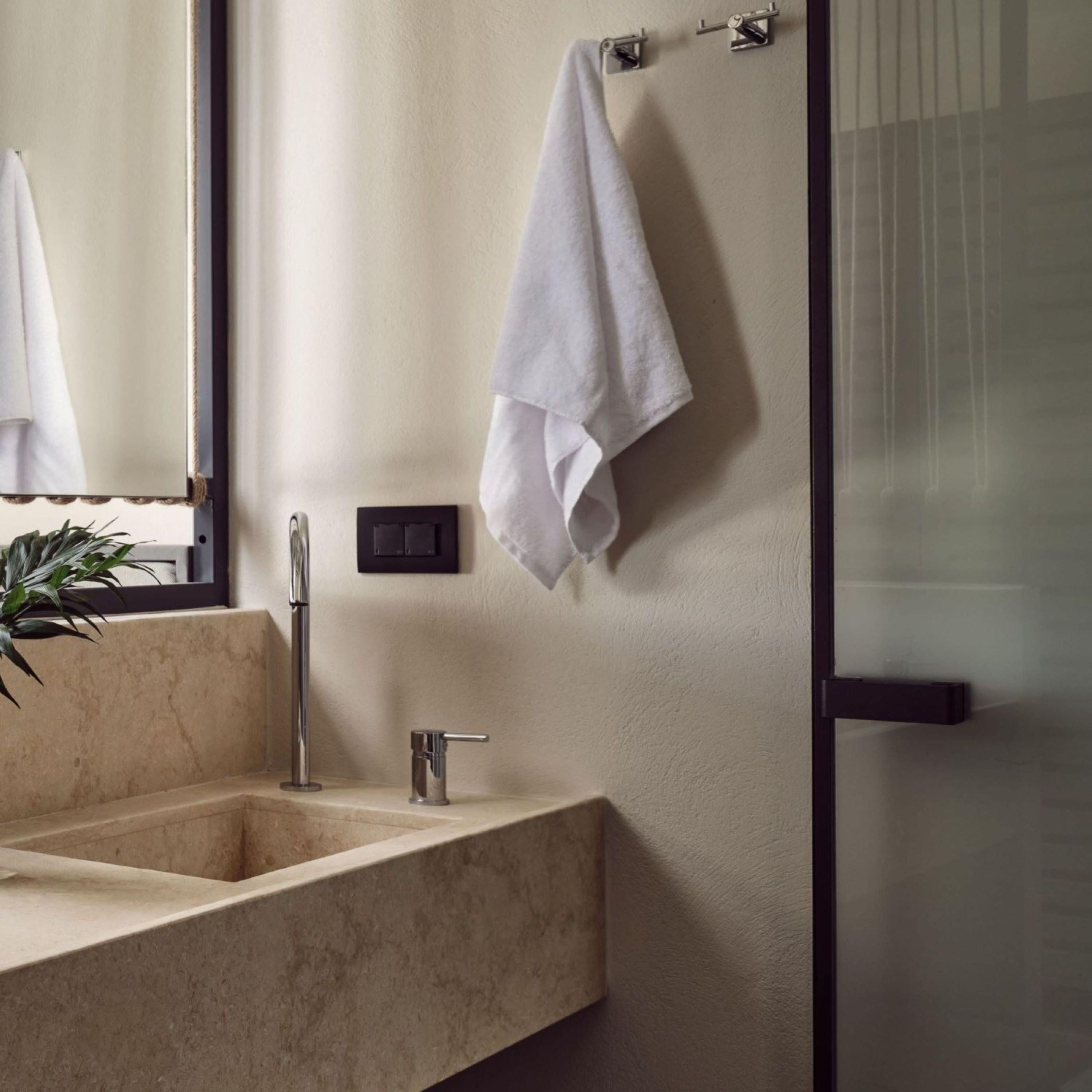 Een badkamer met een marmeren wastafel, een waterkraan, een handdoekhouder en een potplant.