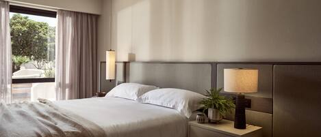 A hotel room with a large bed, bedside tables, a potted plant, and a view of the outdoors.