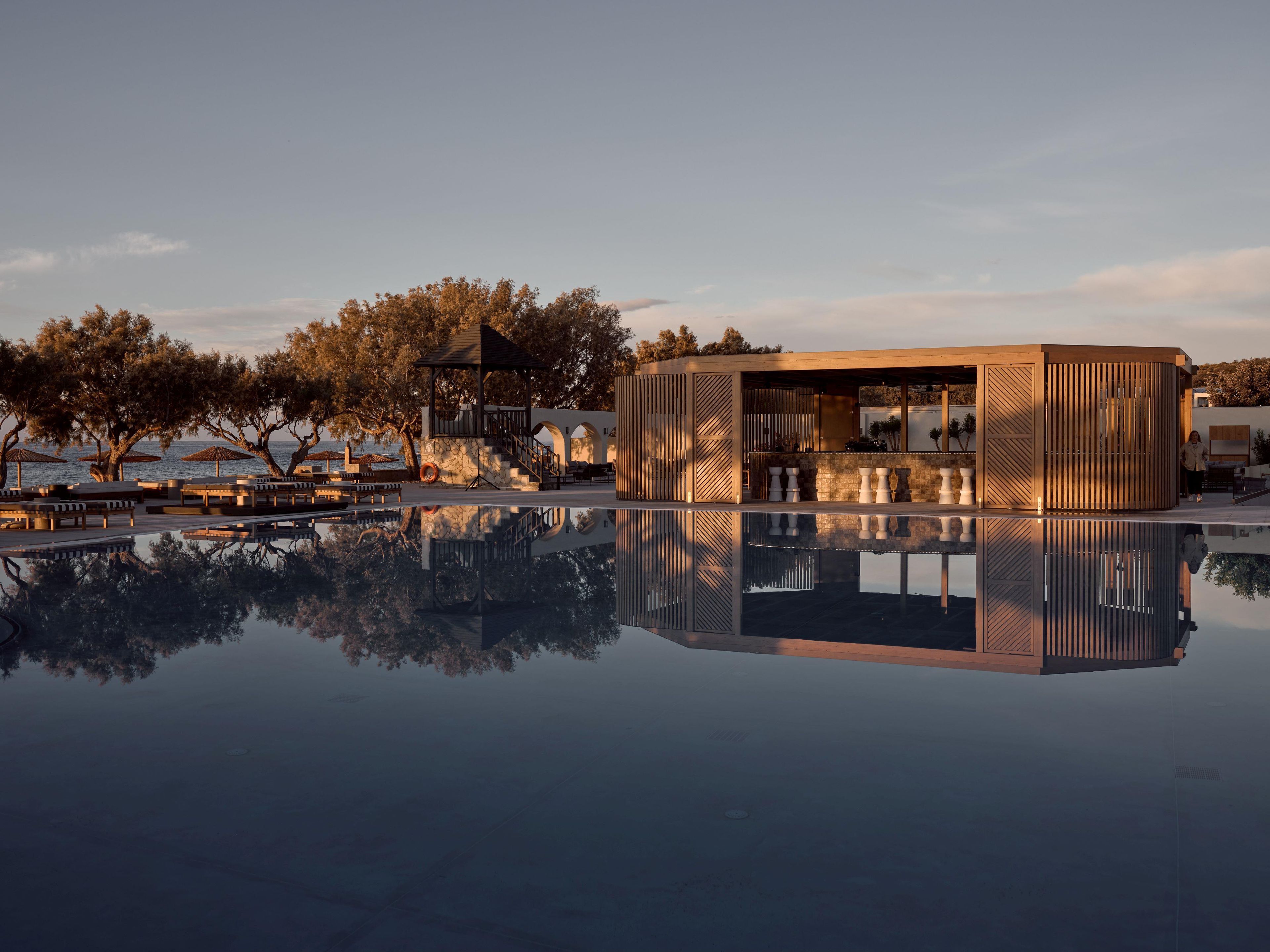 A modern outdoor pool area with a wooden structure, seating, and trees.