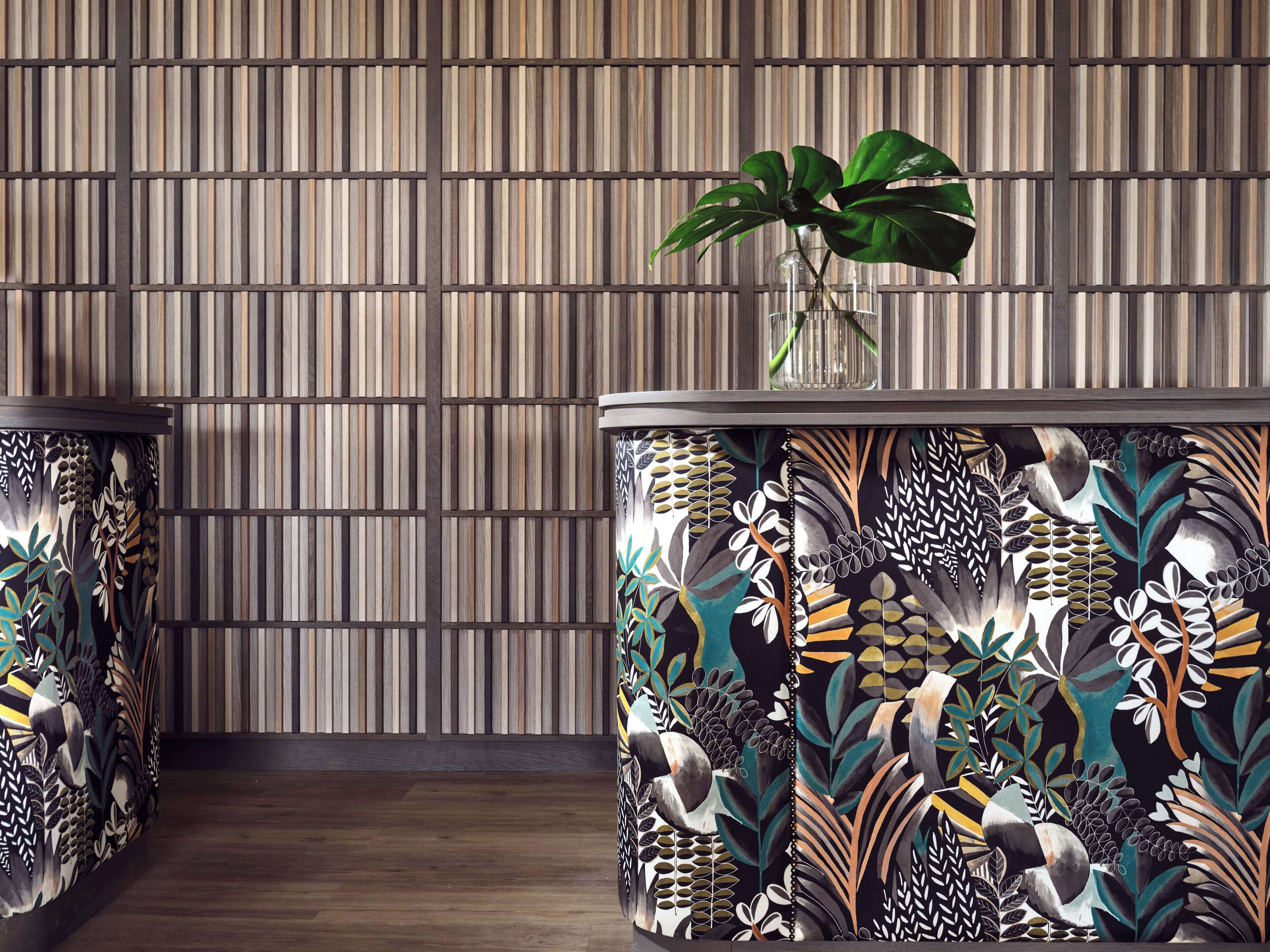 Ein Zimmer mit einer Wand aus Holzstreifen, einer Pflanze in einer Glasvase und einem Beistelltisch mit einem Pflanzenmotiv.