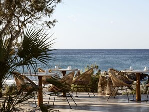 An outdoor seating area with tables and chairs, overlooking the ocean. - Numo Ierapetra Beach Resort Crete, Curio Collection Hilton (Ierapetra)