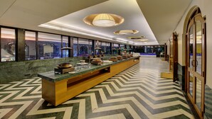 Een moderne hotellobby met een lange receptiebalie, grote ramen en een vloer met een chevrond patroon.