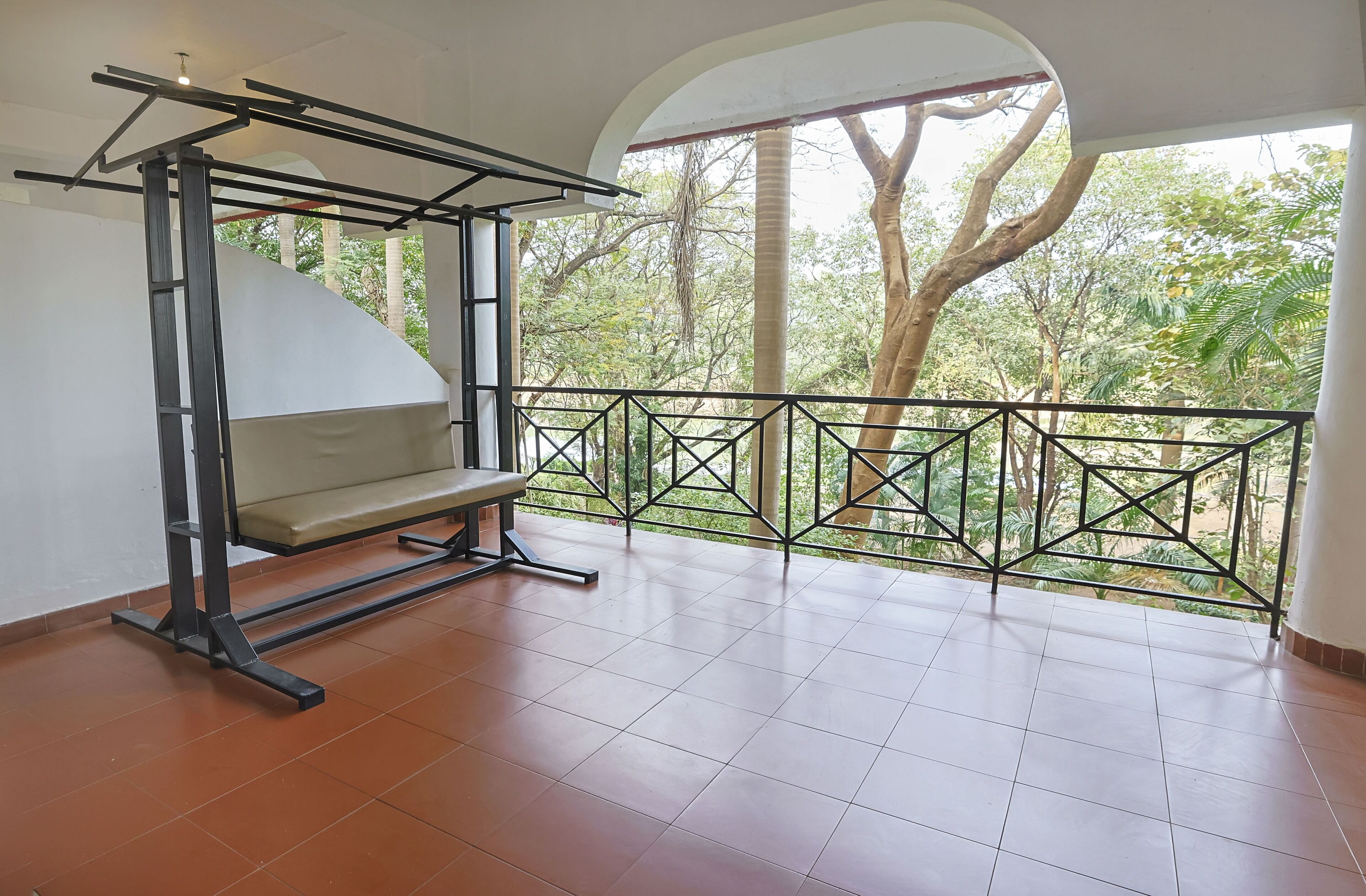 A balcony with a metal railing, a bench, and a view of trees and greenery.