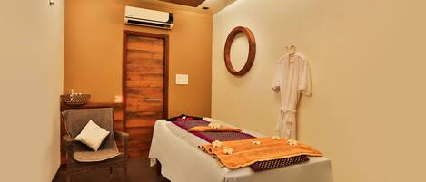 A spa room with a massage table, towels, a chair, and a mirror.