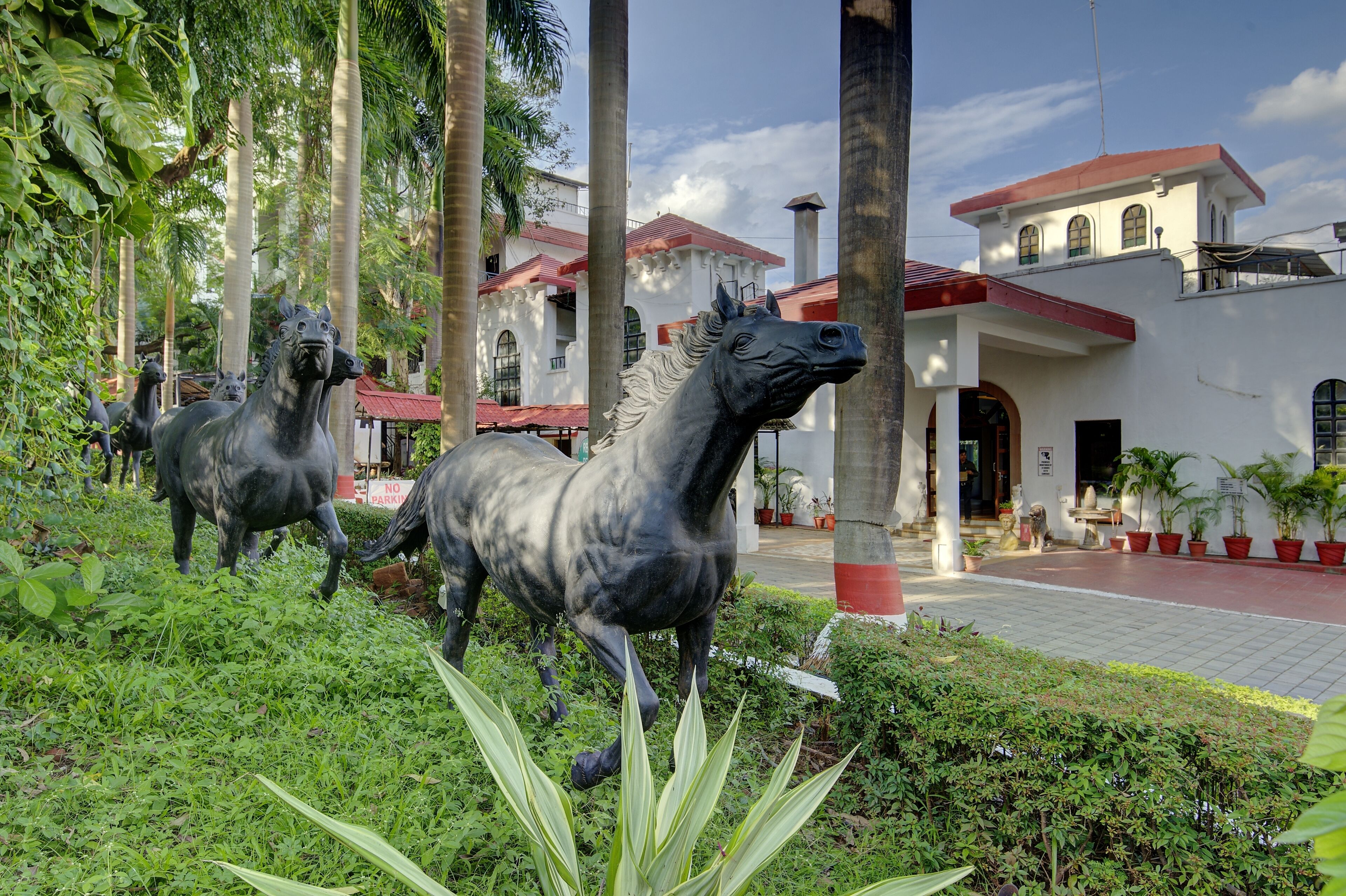 A courtyard with horse statues, palm trees, and a building with a red roof.
