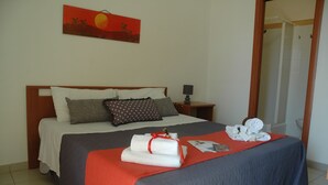 A neatly made bed with a red blanket, pillows, and rolled towels.
