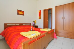 Un dormitorio con una cama de madera, una mesita de noche con una lámpara y un jarrón de girasoles, además de un armario.