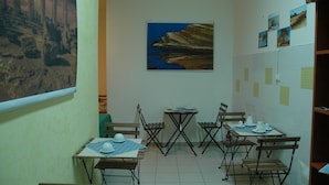 A dining area with foldable tables and chairs, a painting on the wall, and a tiled wall with notes.