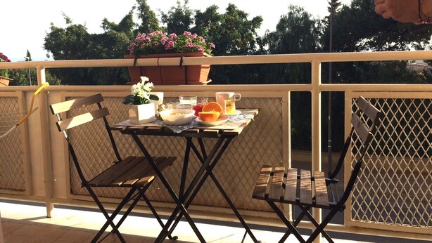 A balcony with a table set for breakfast, including a bowl, orange, and a cup.