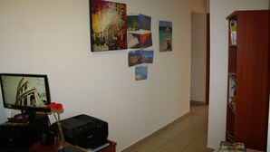 A hallway with a computer monitor, printer, and a vase with a flower on a desk. There are several framed pictures on the wall.