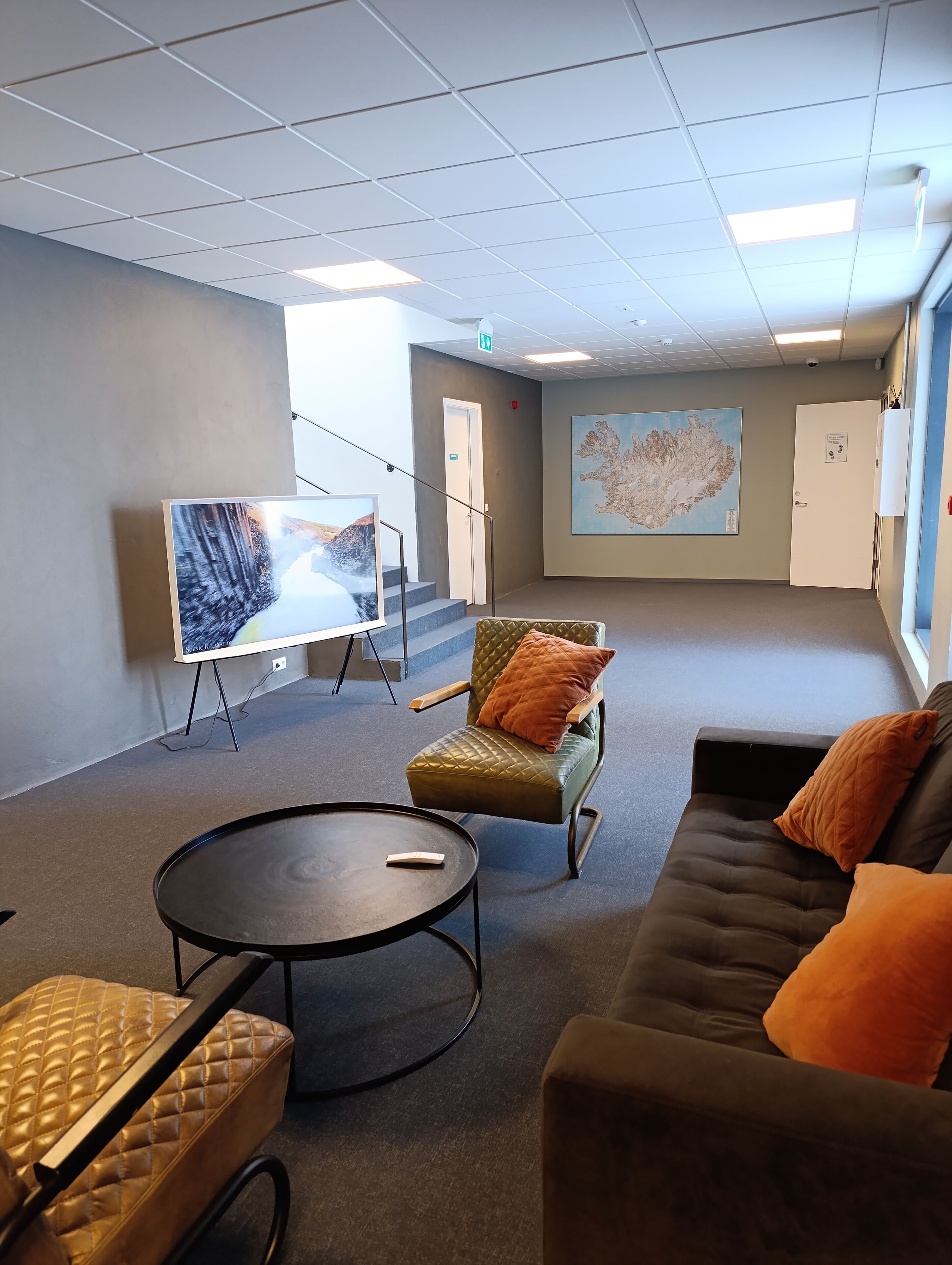Ein moderner Lounge-Bereich mit Flachbildfernseher, gepolstertem Sessel, einer Couch und einem runden Tisch.