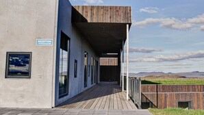 Et receptionsområde med en træterrasse, der fører til en bygning, et skilt der angiver receptionen, og udsigt over landskabet.