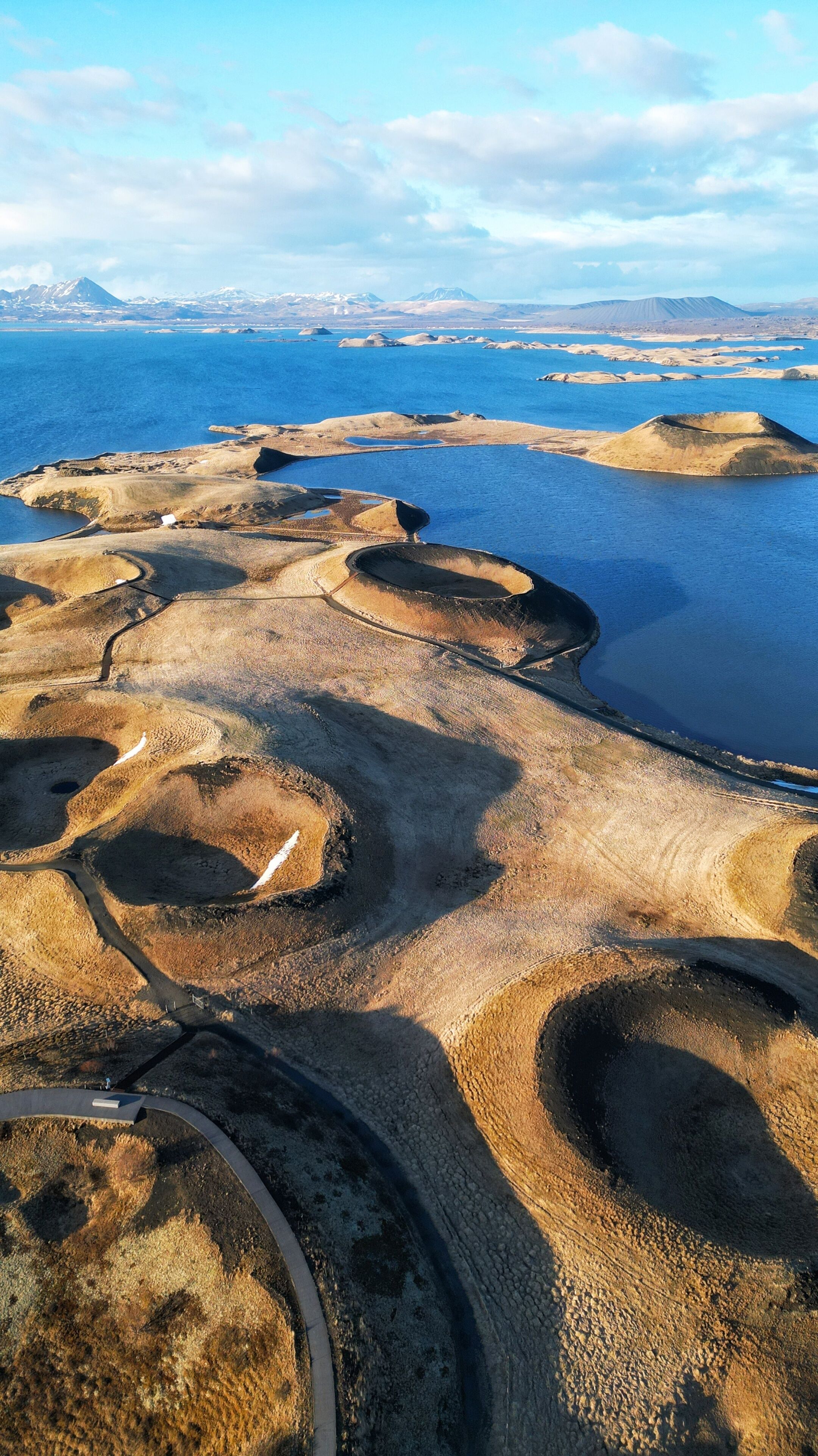 An aerial view of a coastal landscape with distinct geological formations, a road, and a distant mountain range.