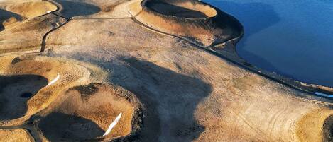 An aerial view of a coastal landscape with distinct geological formations, a road, and a distant mountain range.