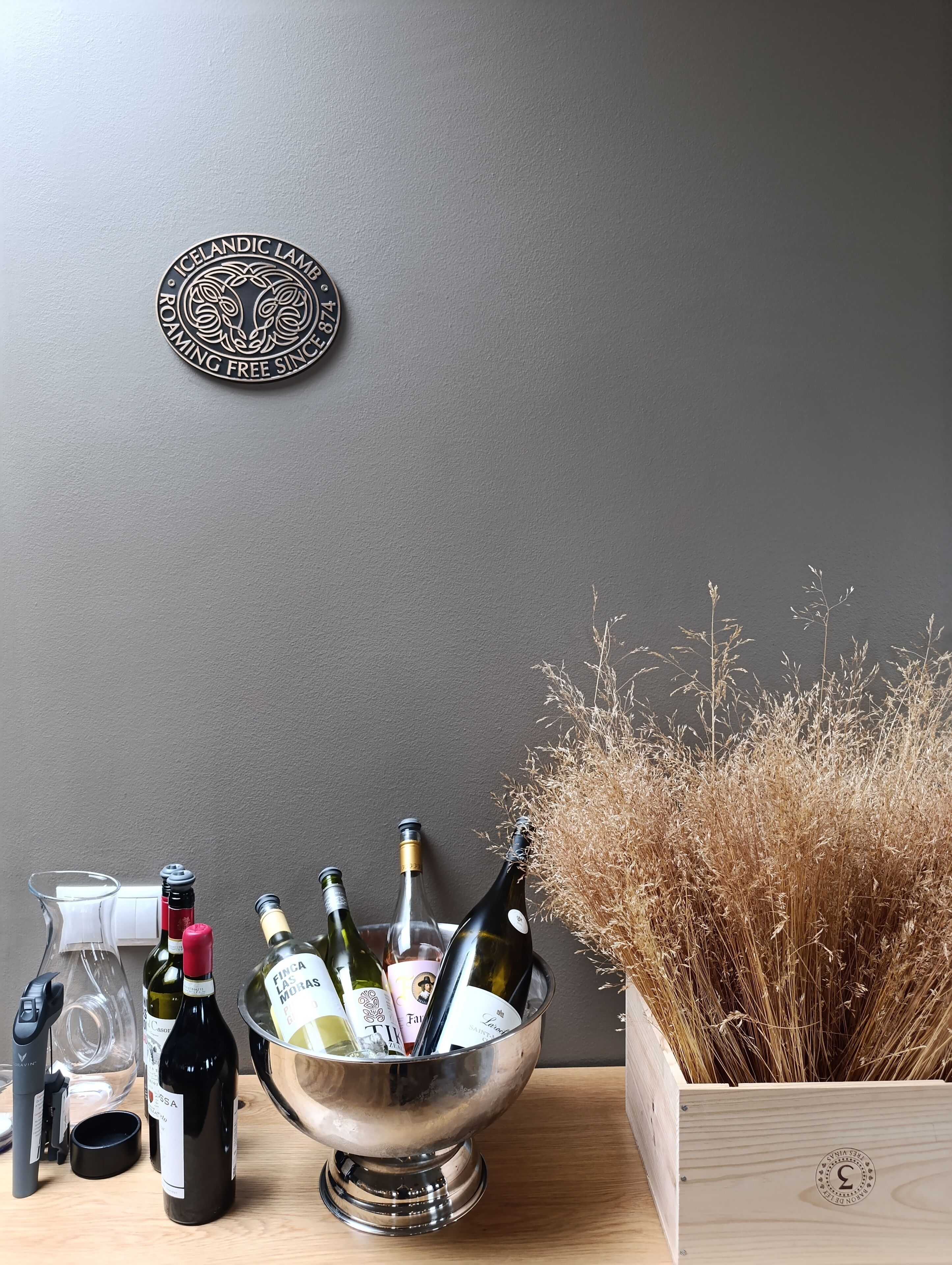 A table with a metal bowl containing wine bottles, a wine opener, and a glass.