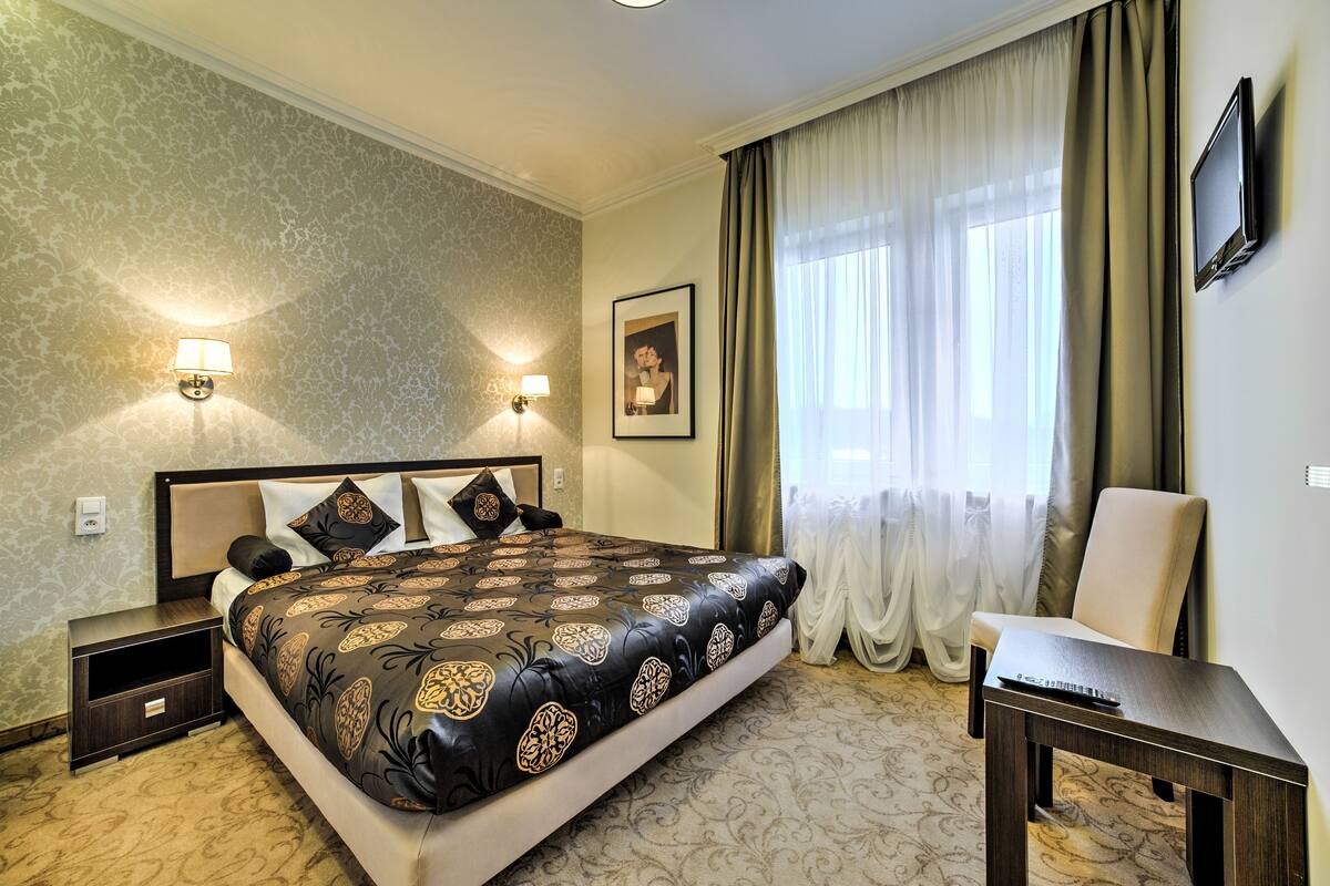 A hotel room with a large bed, two bedside lamps, a flat-screen TV, a chair, and a framed picture on the wall.