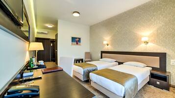 A hotel room with two beds, a desk with a lamp, a coffee maker, and a small table with a book and remote controls.