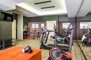Un gimnasio con equipo de ejercicio, un televisor y una banca.