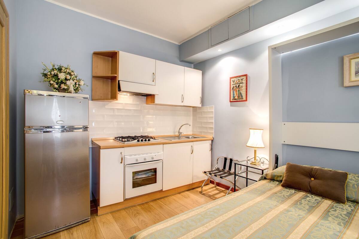A compact kitchen with white cabinets, a stainless steel refrigerator, and a wooden countertop.