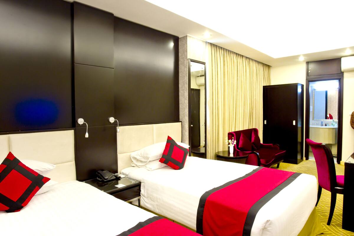 A hotel room with two beds, a desk, a chair, a mirror, and a bathroom visible through an open door.