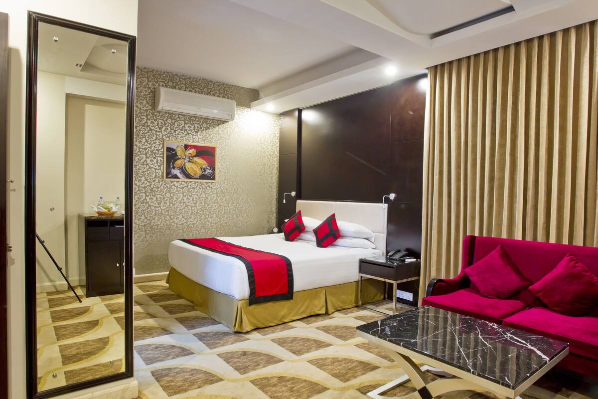 A hotel room with a bed, a nightstand, a red sofa, a coffee table, and a mirror.
