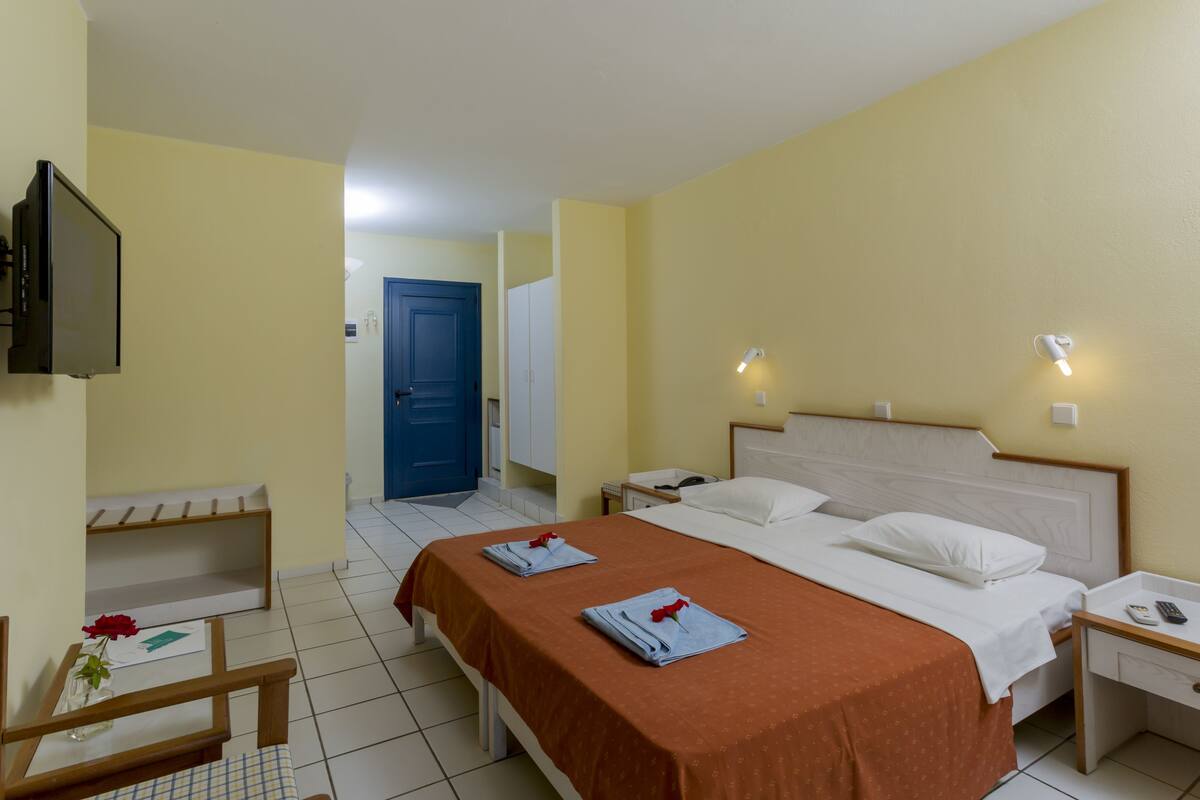 A hotel room with a bed, bedside tables, a TV, and a bathroom visible through an open door.