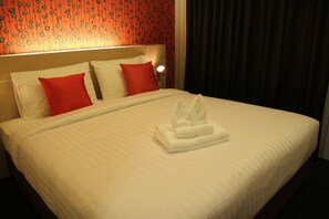 A neatly made bed with white and red pillows, a folded white towel, and a headboard with a floral pattern. - Pakdee Bed and Breakfast (Bangkok)
