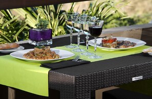 An outdoor dining setup with plates of food, wine glasses, and a decorative purple vase. - Hotel Porta d'Alella (Alella)