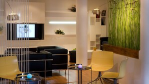 A modern living room with a sectional sofa, a yellow armchair, a small round table with a blue object, and a tall plant. - Hotel Porta d'Alella (Alella)