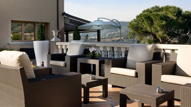 A terrace with wicker furniture, a table, and a view of the landscape. - Hotel Porta d'Alella (Alella)