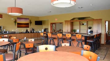 Un restaurant avec plusieurs tables et chaises, un comptoir avec une machine à café et un téléviseur fixé au mur.