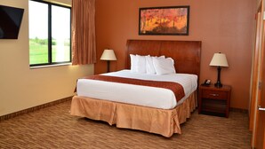 A hotel room with a large bed, two bedside tables with lamps, a flat-screen TV mounted on the wall, and a painting above the bed. - Cobblestone Inn & Suites - Newton (Newton)