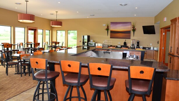 A spacious kitchen with a large island, bar stools, and a flat-screen TV mounted on the wall. - Cobblestone Inn & Suites - Newton (Newton)