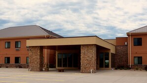 A hotel entrance with a covered waiting area, stone pillars, and a parking lot. - Cobblestone Inn & Suites - Newton (Newton)