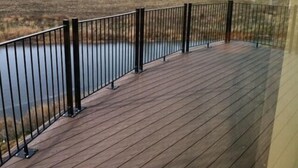 A wooden deck with a metal railing overlooking a body of water and a grassy landscape. - Cobblestone Inn & Suites - Newton (Newton)