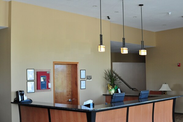 A reception area with a wooden reception desk, a coffee machine, a plant, and a sign indicating the check-out desk.