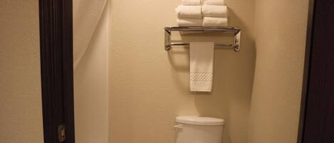 A small bathroom with a toilet, a towel rack with folded towels, a trash can, and a bathtub.