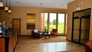 A hotel lobby with a reception desk, seating area, large windows, and an exit sign. - Cobblestone Inn & Suites - Newton (Newton)